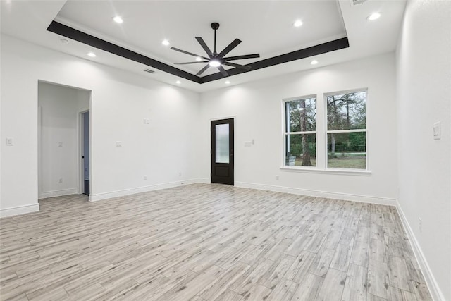 unfurnished living room with ceiling fan, a raised ceiling, and light hardwood / wood-style flooring