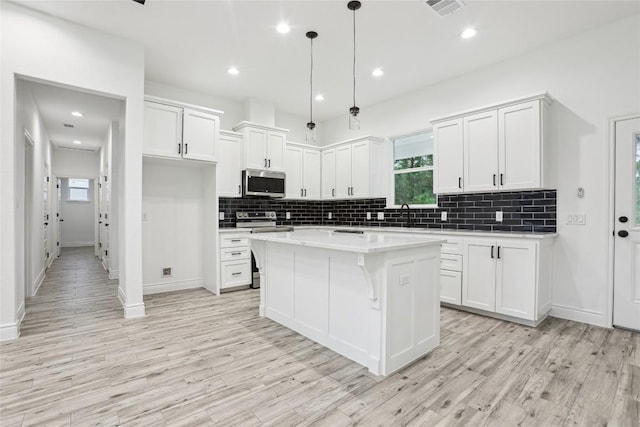kitchen featuring pendant lighting, stainless steel appliances, white cabinets, and a kitchen island
