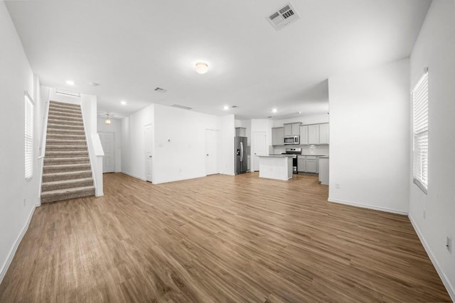 unfurnished living room with stairway, wood finished floors, visible vents, and baseboards