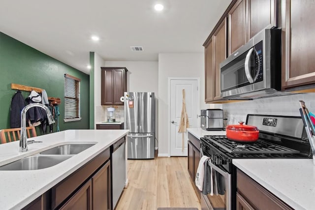 kitchen with sink, light hardwood / wood-style flooring, stainless steel appliances, light stone counters, and tasteful backsplash