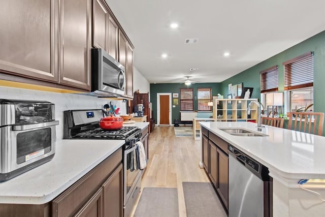 kitchen featuring appliances with stainless steel finishes, sink, a kitchen island with sink, ceiling fan, and light hardwood / wood-style floors