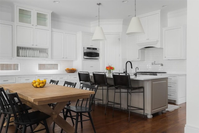 kitchen with white cabinets, a kitchen bar, ornamental molding, a kitchen island with sink, and stainless steel oven