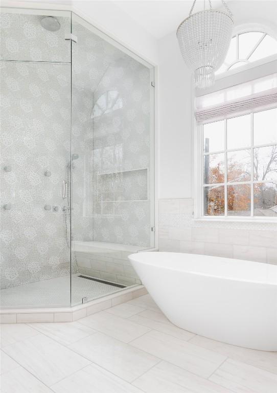 bathroom featuring plus walk in shower, tile walls, and an inviting chandelier