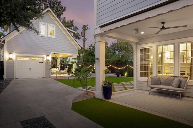 patio terrace at dusk with ceiling fan, a garage, and a yard