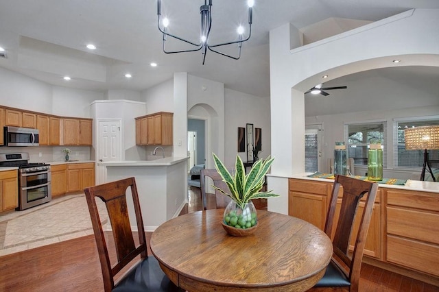 dining room with ceiling fan with notable chandelier, a towering ceiling, sink, and light hardwood / wood-style floors