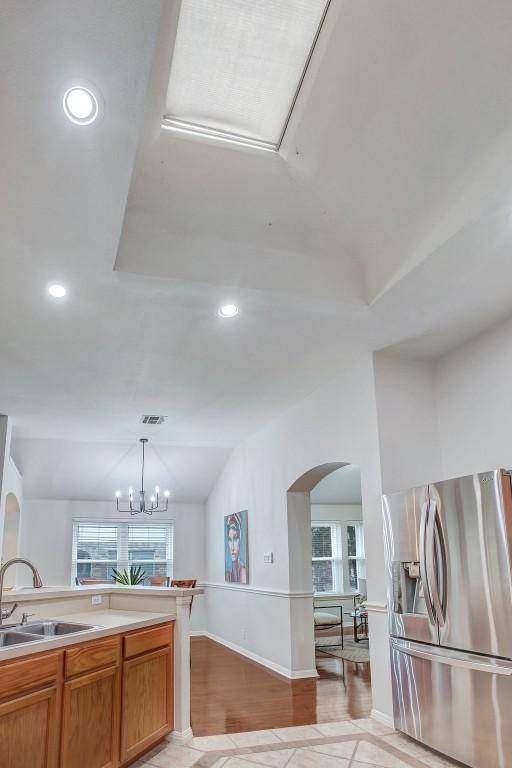 kitchen featuring sink, decorative light fixtures, vaulted ceiling, stainless steel fridge with ice dispenser, and a notable chandelier