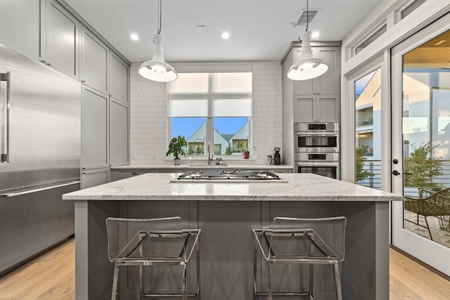 kitchen featuring stainless steel appliances, a breakfast bar, light stone counters, and gray cabinets