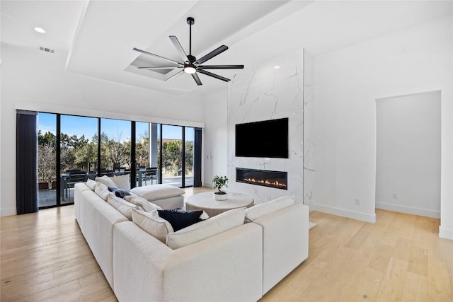 living room with a high ceiling, ceiling fan, a fireplace, and light hardwood / wood-style floors