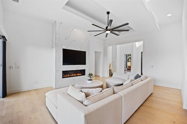 living room with a high end fireplace, light hardwood / wood-style floors, and a raised ceiling