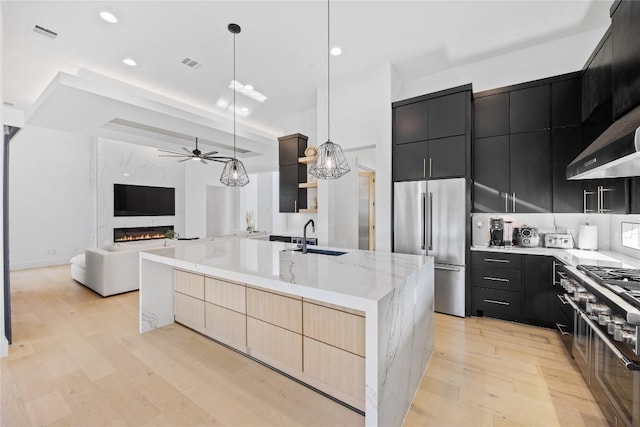 kitchen with pendant lighting, sink, premium appliances, a high end fireplace, and an island with sink