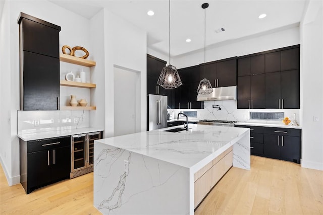 kitchen featuring sink, a kitchen island with sink, decorative light fixtures, high end refrigerator, and exhaust hood