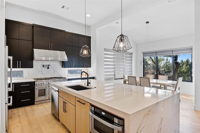 kitchen with appliances with stainless steel finishes, pendant lighting, an island with sink, sink, and decorative backsplash