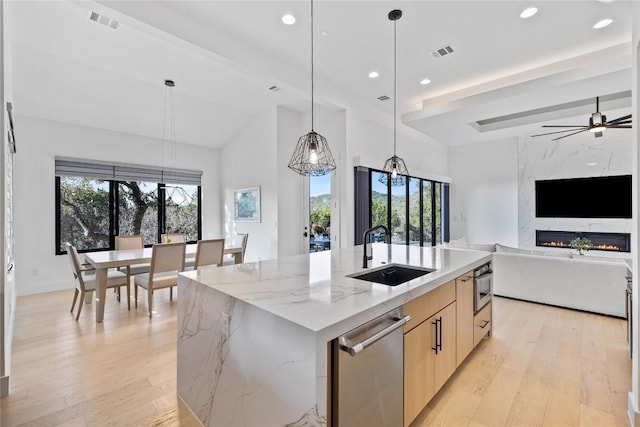 kitchen with pendant lighting, sink, a kitchen island with sink, a high end fireplace, and light stone counters