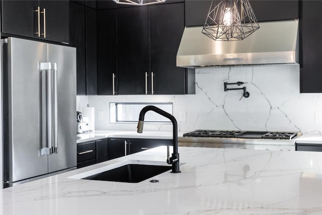 kitchen with extractor fan, decorative light fixtures, sink, light stone counters, and stainless steel appliances