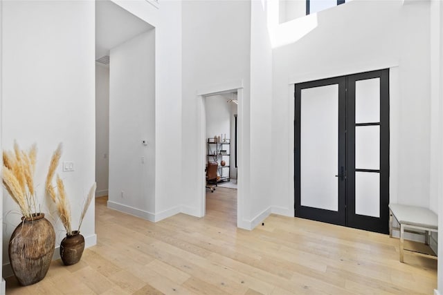 foyer entrance featuring french doors, light hardwood / wood-style flooring, and a high ceiling