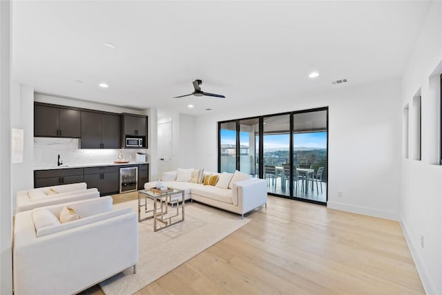 living room featuring ceiling fan, sink, beverage cooler, and light wood-type flooring