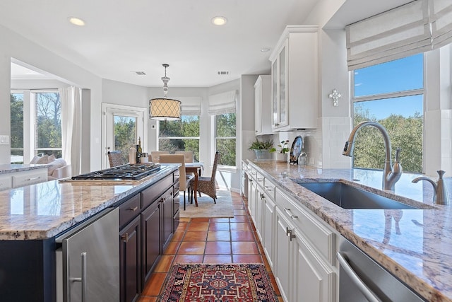 kitchen with appliances with stainless steel finishes, white cabinetry, sink, decorative backsplash, and light stone countertops