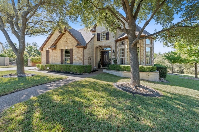 french country home with stone siding, roof with shingles, fence, a front lawn, and brick siding