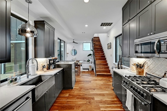 kitchen with decorative light fixtures, light hardwood / wood-style flooring, decorative backsplash, and appliances with stainless steel finishes