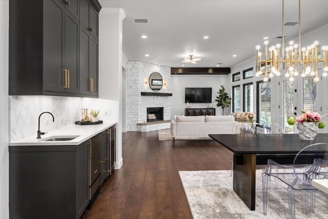 dining space featuring dark wood-type flooring, sink, ornamental molding, a notable chandelier, and a fireplace