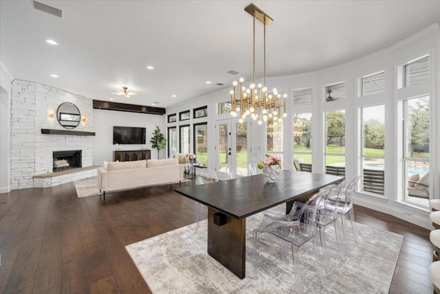 dining area with dark wood-type flooring, ornamental molding, and a stone fireplace