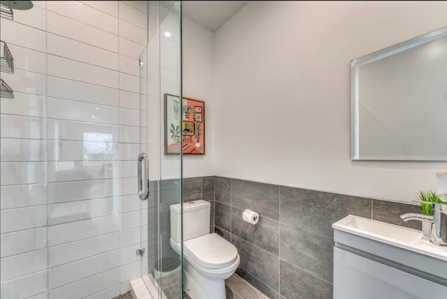 bathroom with a shower with door, vanity, tile walls, and toilet