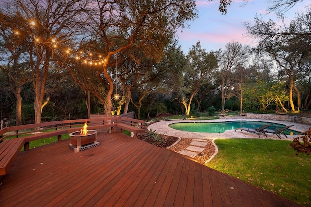 pool at dusk featuring a lawn, a deck, and a fire pit