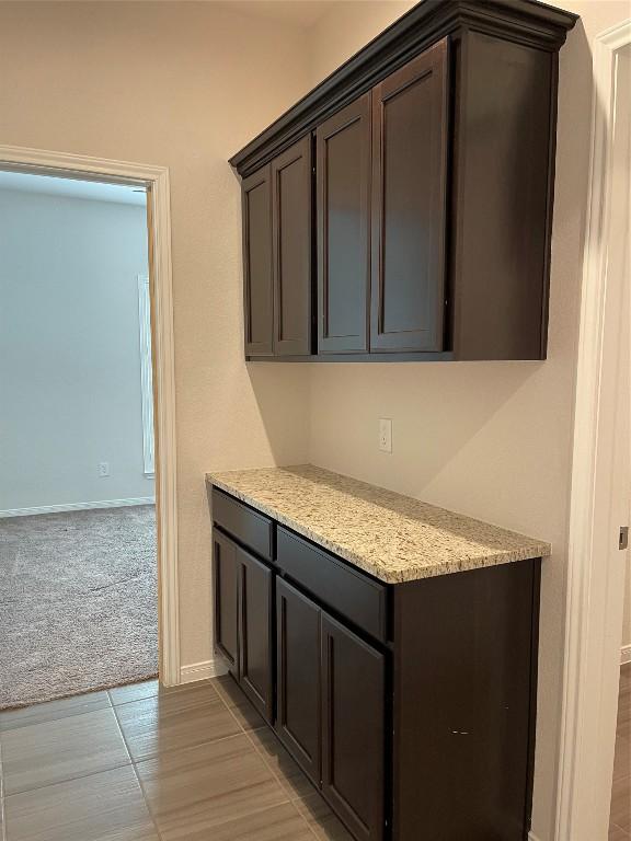 kitchen with dark brown cabinets, light stone countertops, and light carpet