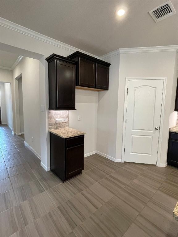 kitchen with light stone counters, crown molding, and dark brown cabinets