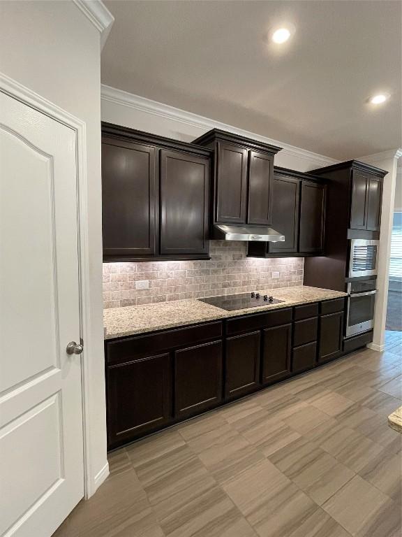 kitchen featuring dark brown cabinetry, ornamental molding, stainless steel appliances, light stone countertops, and backsplash