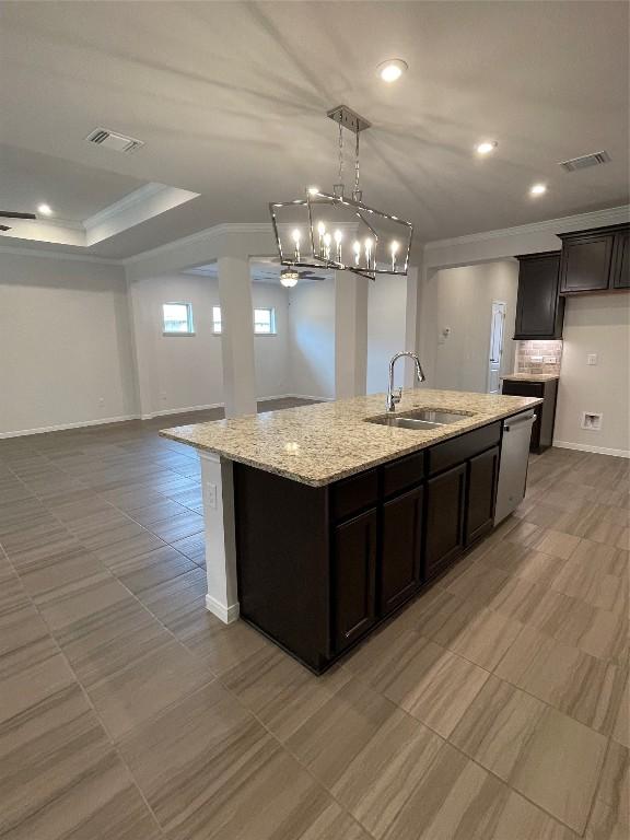 kitchen featuring dishwasher, sink, ornamental molding, a kitchen island with sink, and light stone counters