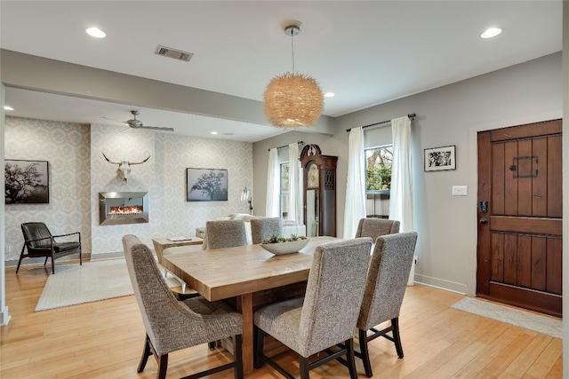 dining space featuring ceiling fan, a large fireplace, and light wood-type flooring