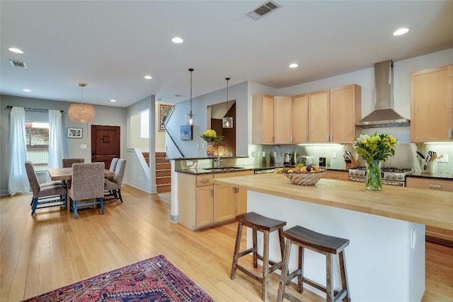 1109 Holly St Unit B, Austin, TX 78702 - kitchen featuring wall chimney exhaust hood, light brown cabinetry, butcher block countertops, light wood-style flooring, and a kitchen bar