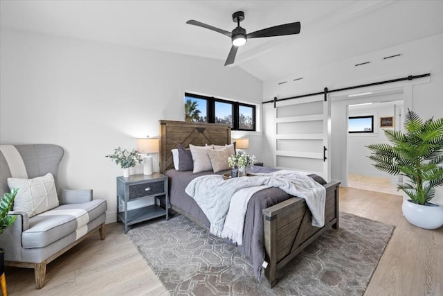 bedroom featuring ceiling fan, wood-type flooring, a barn door, and vaulted ceiling with beams