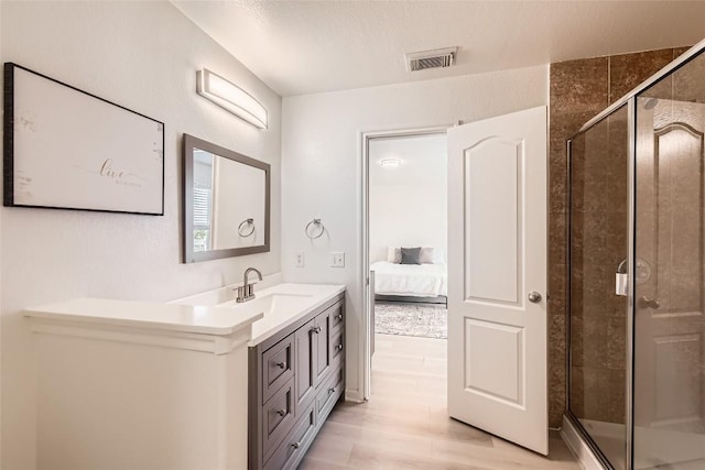 ensuite bathroom featuring visible vents, a stall shower, vanity, ensuite bath, and wood finished floors