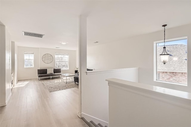 corridor featuring baseboards, visible vents, light wood finished floors, and an upstairs landing