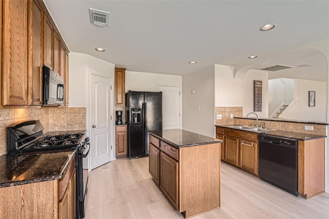 kitchen with visible vents, a kitchen island, a sink, black appliances, and light wood-type flooring