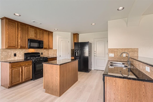 kitchen with a peninsula, black appliances, dark stone counters, and a sink