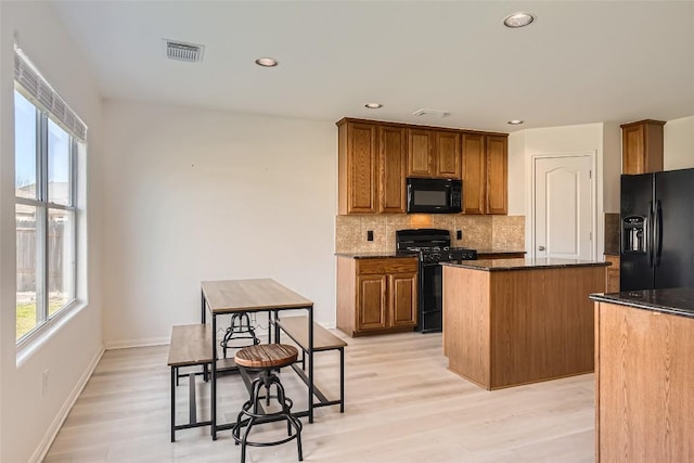 kitchen featuring plenty of natural light, dark stone countertops, a center island, black appliances, and backsplash