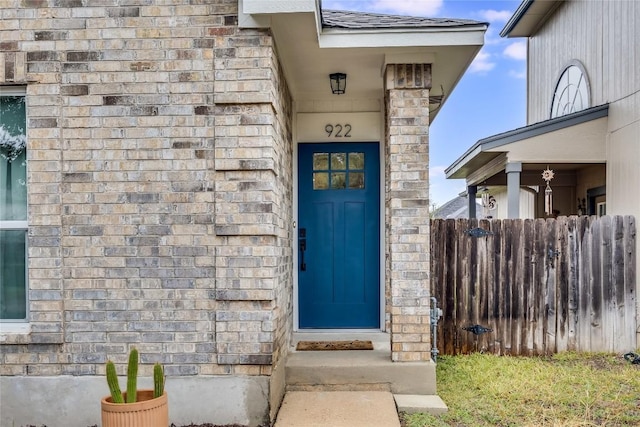 entrance to property featuring fence, roof with shingles, and stone siding