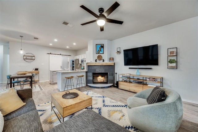 living room featuring light wood finished floors, visible vents, a barn door, ceiling fan, and baseboards