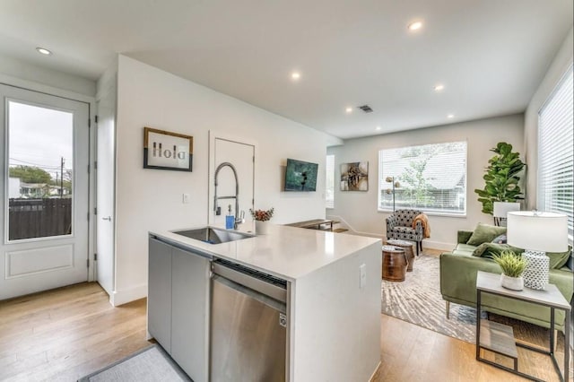 kitchen featuring stainless steel dishwasher, light hardwood / wood-style floors, sink, and a center island with sink