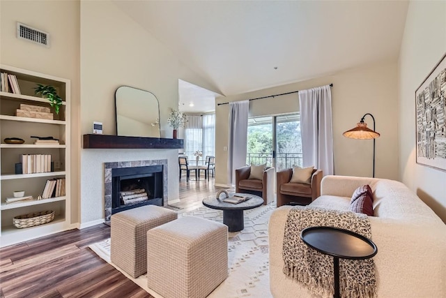 living room featuring wood-type flooring, a tiled fireplace, and high vaulted ceiling