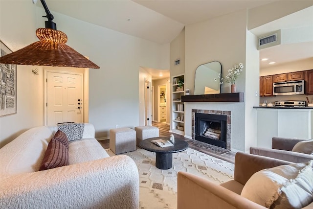 living room with built in shelves, a fireplace, high vaulted ceiling, and light wood-type flooring