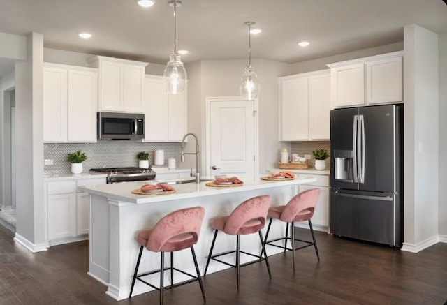 kitchen featuring white cabinetry, decorative light fixtures, a center island with sink, dark hardwood / wood-style floors, and stainless steel appliances