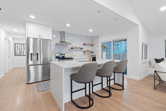 kitchen with wall chimney range hood, sink, a breakfast bar area, stainless steel appliances, and white cabinets