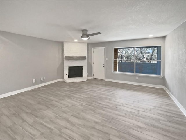 unfurnished living room featuring ceiling fan, light hardwood / wood-style floors, a brick fireplace, and a textured ceiling