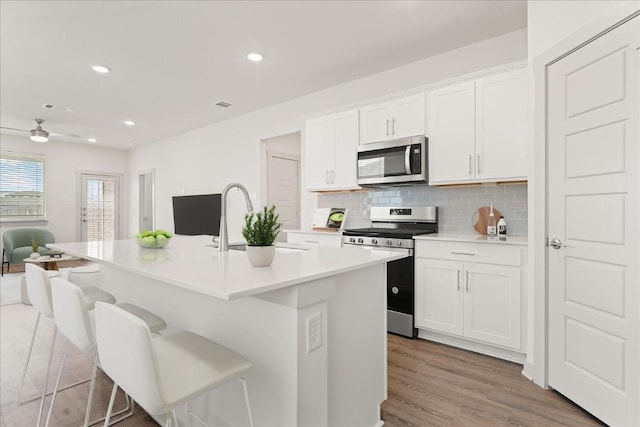 kitchen with white cabinetry, sink, stainless steel appliances, and a center island with sink