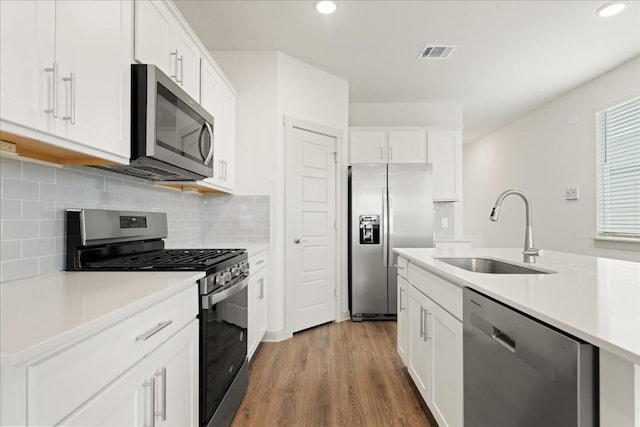 kitchen featuring hardwood / wood-style floors, white cabinetry, sink, decorative backsplash, and stainless steel appliances