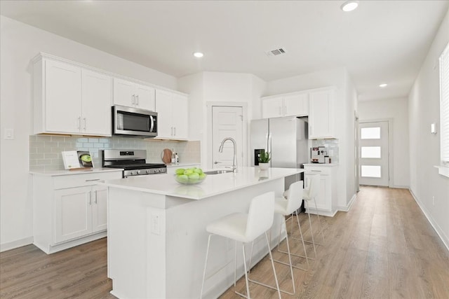 kitchen with appliances with stainless steel finishes, a center island with sink, and white cabinets